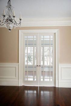 an empty room with wood floors and chandelier hanging from the ceiling in front of two doors