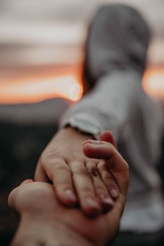 two people holding hands with the sun setting in the back ground behind them, and one person's arm wrapped around him