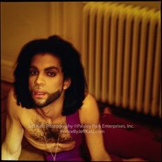 a man with long hair and beard sitting on the floor next to a radiator