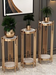 three gold and white plant stands in front of a wall with a painting on it