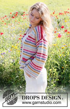 a woman is standing in the middle of a flower field wearing a colorful striped cardigan