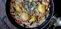 a stew with potatoes, carrots and other vegetables in a black bowl on a wooden table