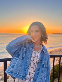 a woman standing on top of a balcony next to the ocean at sun set with her hands in her hair