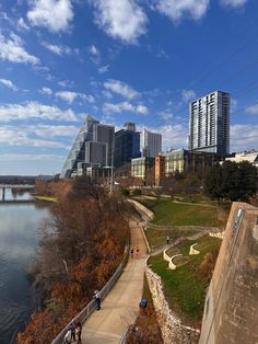 people walking along the edge of a river with tall buildings in the background on a sunny day