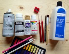 the supplies needed for painting are laid out on top of a wooden table, including paints and pencils