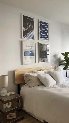 a bed with white linens and pillows in a bedroom next to a mirror, lamp and pictures on the wall