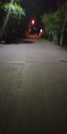 an empty street at night with no cars or people on the road and trees in the background