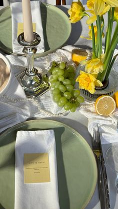 the table is set with yellow flowers and green grapes