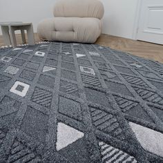 a grey rug with white and black designs on it next to a beige chair in front of a door