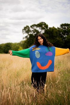 a woman standing in a field with her arms spread out to the side, wearing a colorful sweater