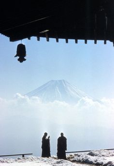 two people standing in the snow looking at a mountain