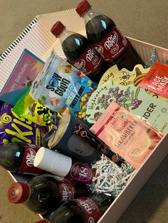 a box filled with drinks and snacks on top of a carpeted floor in front of a wall