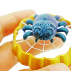 a hand holding a plastic toy with a blue spider on it's back and yellow rim