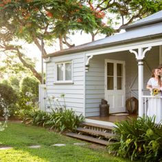 a bride and groom standing on the porch of their white picket house with trees in the background