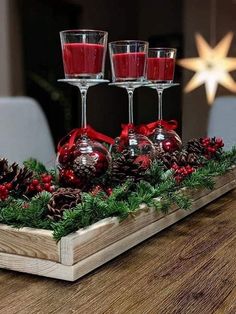 three wine glasses are sitting on a tray with pine cones and berries