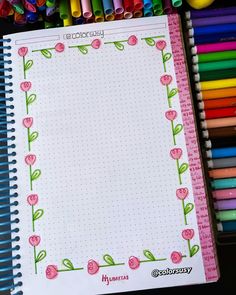 an open notebook with pink flowers on it and colored crayons in the background