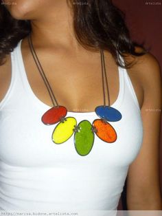 a woman wearing a white tank top with colorful necklaces on it's neck