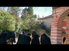 several people in black robes are walking through an archway with trees and buildings behind them