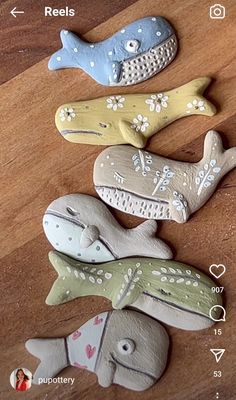 four ceramic fish on a wooden table with hearts and arrows in the middle one is blue, green, yellow, and white