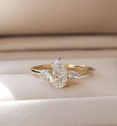 an engagement ring with three pear shaped diamonds on it's side, sitting in a box