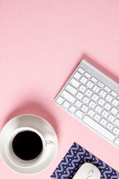 a cup of coffee next to a keyboard and mouse on a pink surface with an envelope