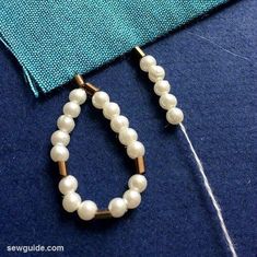 a pair of white beaded hoop earrings sitting on top of a piece of fabric