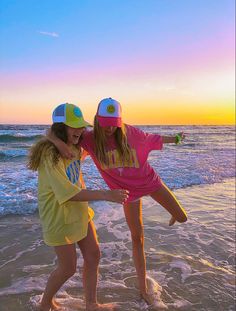 two girls are playing on the beach at sunset