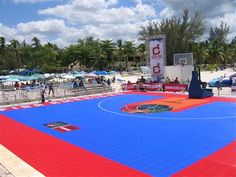 an outdoor basketball court is painted red, blue and white with people standing around it