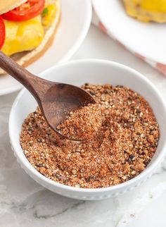 a wooden spoon in a white bowl filled with ground spices next to burgers on plates