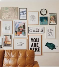 a brown leather couch sitting in front of a wall covered with pictures and framed art