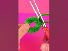 someone is making a green wreath out of yarn and knitting needles with the help of scissors