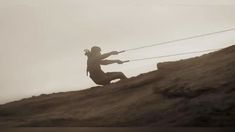 a man is climbing up the side of a hill with rope attached to his back