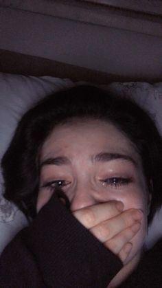 a woman laying in bed with her eyes closed and covering her face from the sun