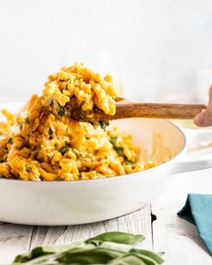 a spoon full of macaroni and cheese being lifted from a white bowl on top of a wooden table