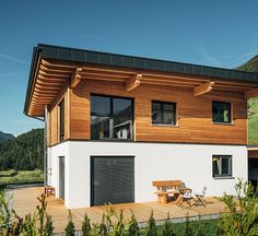 a modern house with wooden siding and black shutters on the windows, overlooking a green hillside