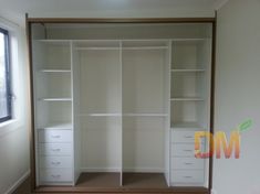 an empty closet with white shelves and drawers in the corner, next to a window