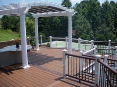 a wooden deck with white railings and pergolated area on the side of it