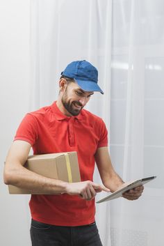 a man in a red shirt and blue cap is holding a box while looking at something