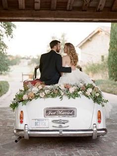 a bride and groom are sitting in the back of an old car with flowers on it