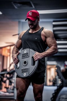 a man in shorts and a red hat holding a weight plate with his hands on it