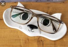 a pair of glasses sitting on top of a white cat shaped object with green eyes