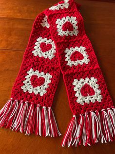 a crocheted scarf with white and red trims on a wooden table top