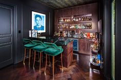 a bar with stools and bottles on the shelves in a room that has dark wood flooring