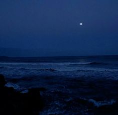 the moon is setting over the ocean with waves coming in to shore and dark blue sky