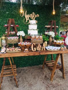 a table topped with cakes and cupcakes on top of wooden tables covered in greenery