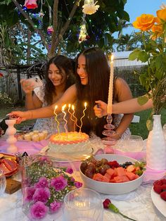 two women sitting at a table with cake and candles in front of them, surrounded by flowers