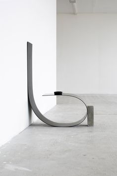 a metal sculpture sitting on top of a cement floor next to a white wall in an empty room