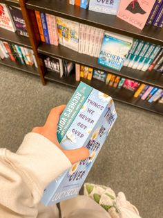 a person is holding a book in front of a bookshelf full of books