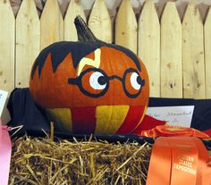 a pumpkin with glasses on it sitting in hay next to a fence and orange ribbon