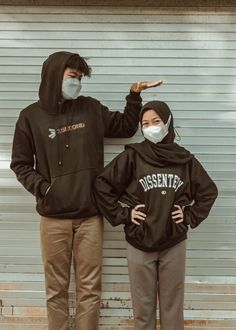 two people wearing face masks standing next to each other in front of a garage door